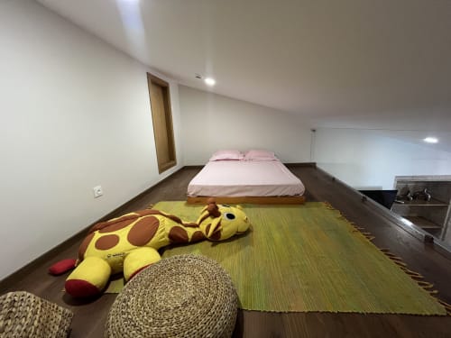 Espaçoso quarto tipo loft na RISOTURISMO com cama rosa, girafa de pelúcia amarela e tapete tecido sobre piso de madeira escura