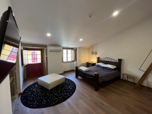 Quarto espaçoso no Quarto Massena com cama preta, puff branco, piso em madeira escura e comodidades modernas incluindo TV e