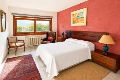 Amplia habitación familiar en Hacienda Blanca Marbella con paredes rojas, cama de madera, sillón y vistas a la terraza