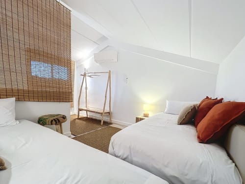 Dormitorio moderno en la casa rural Estartit con camas gemelas, almohadas naranjas, perchero de madera y luz natural