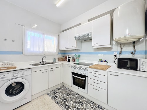 Cocina blanca moderna con acentos de azulejos azules, electrodomésticos de acero inoxidable y suelo con patrón en La Estartit