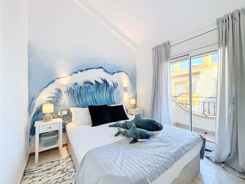 Dormitorio moderno en Estartit con mural de olas oceánicas, ropa de cama blanca y vistas al balcón en L'Estartit