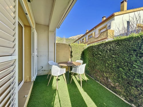 Patio privado de la casita La Vela en L'Estartit con mesa de comedor, sillas blancas y seto de privacidad
