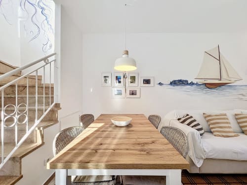 Comedor de cabaña costera luminosa con mesa de madera, arte de velero en la pared y cojines a rayas en la habitación La Vela de Estartit