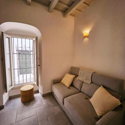 Acogedor estudio en Casa De La Cruz Vejer con sofá cama gris, cojines amarillos, puerta arqueada hacia el patio, cálido