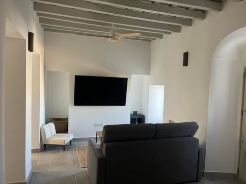 Sala moderna del apartamento Casa De La Cruz Vejer con sofá negro, TV mural, vigas vistas y diseño contemporáneo