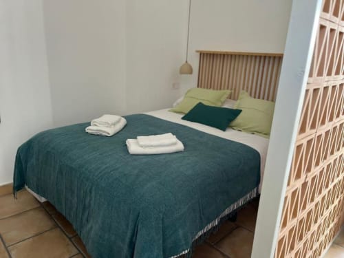 Acogedora habitación en Casa De La Cruz Vejer con colcha azul verdoso, almohadas verdes, cabecero de madera y toallas dobladas sobre la cama