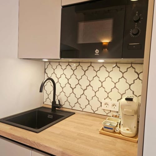 Cocina moderna con microondas negro, azulejos geométricos, encimera de madera y electrodomésticos en Casa De La Cruz Vejer