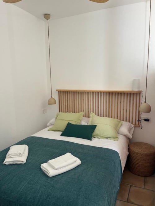 Dormitorio moderno en Casa De La Cruz Vejer con cabecero de madera, ropa de cama verde y amarilla, lámparas colgantes y piso de baldosas