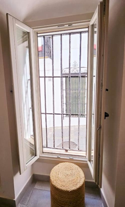 Puerta blanca abierta hacia estudio amueblado con patio y vistas de la ciudad en Vejer de la Frontera, con mesa redonda tejida y ventana