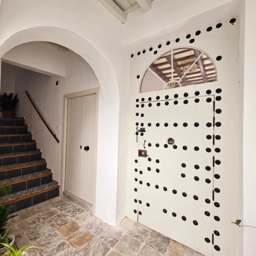 Entrada luminosa de Casa De La Cruz Vejer con puerta arqueada, pared blanca decorada con puntos negros y escaleras en Vejer de la