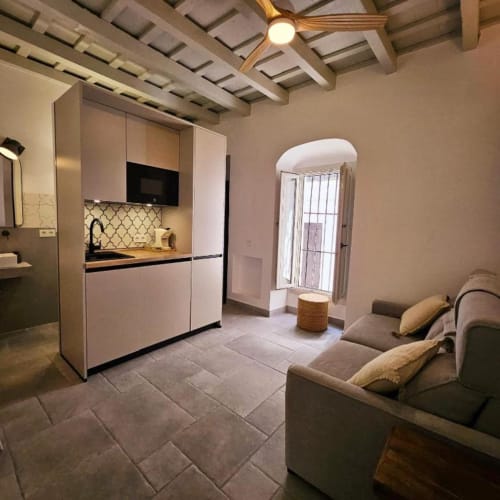 Estudio en Casa De La Cruz Vejer con cocina blanca, sofá cama, vigas vistas y puerta arqueada al patio