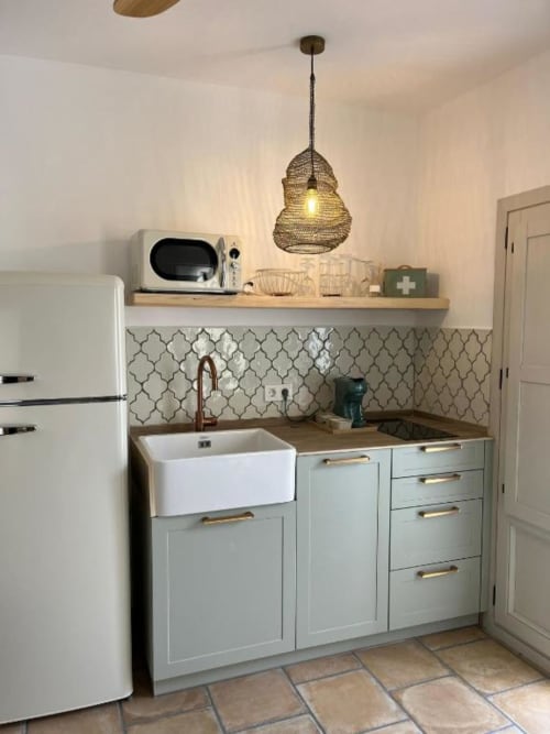 Cocina moderna con alacenas verde salvia, fregadero estilo granja blanco, azulejos decorativos y lámpara colgante tejida en Casa De La