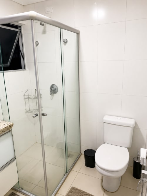 Banheiro moderno no apartamento 305 CSS, Matinhos, com chuveiro de vidro, azulejos brancos, sanitário e comodidades