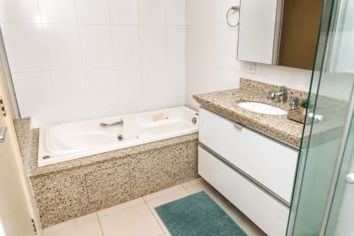 Banheiro moderno da CSS B&B em Matinhos com bancada em granito, banheira branca, pia e box de vidro na Suíte 305