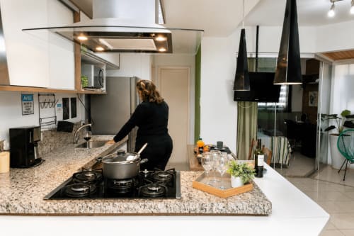 Mulher cozinhando na cozinha moderna do apartamento CSS Planetarium, Matinhos Brasil. Bancadas em granito, fogão a gás, planta aberta.