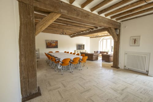 Salle à manger spacieuse de la Villa Chateaudine avec poutres apparentes, carrelage pierre, chaises orangées et vue sur le jardin à Accolade