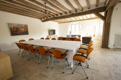 Salle à manger contemporaine à la Villa Chateaudine avec poutres en bois, table en marbre, chaises orange et vue sur le jardin