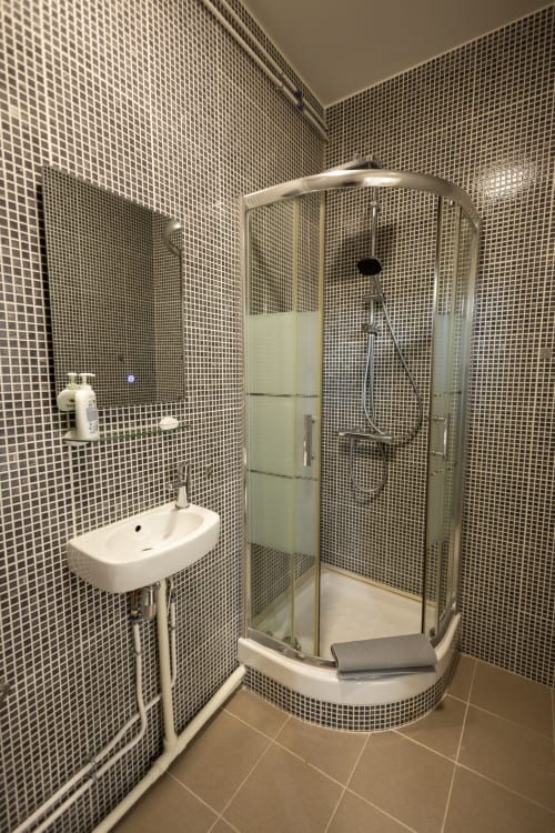 Salle de bain moderne avec petit lavabo et douche vitrée incurvée, carrelage blanc en mosaïque, villa Accolade hotel