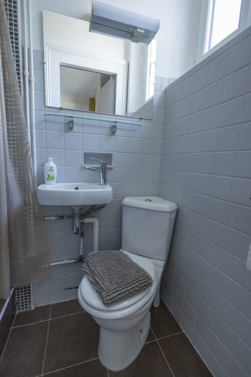 Salle de bain moderne à Accolade Villa Chateaudine avec toilettes blanches, lavabo mural, miroir et carrelage gris
