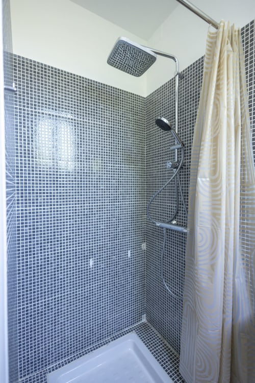 Salle de bain moderne à l'hôtel Accolade avec carrelage mosaïque gris, pomme de douche effet pluie et rideau rayé crème à Villa