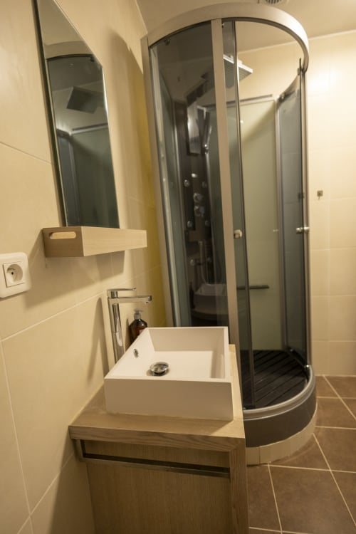 Salle de bains moderne à la Villa Chateaudine de l'hôtel Accolade avec vasque blanche, meuble-lavabo en bois, douche panoramique et