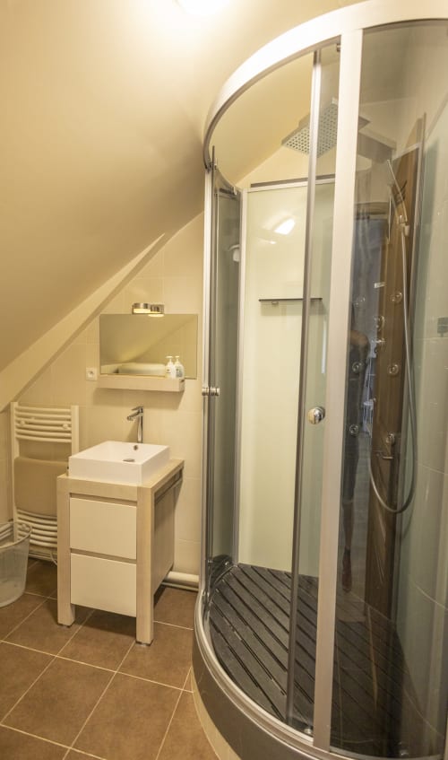 Salle de bain moderne à la Villa Chateaudine de l'hôtel Accolade avec paroi de douche en verre incurvé, vasque blanche et chauffée