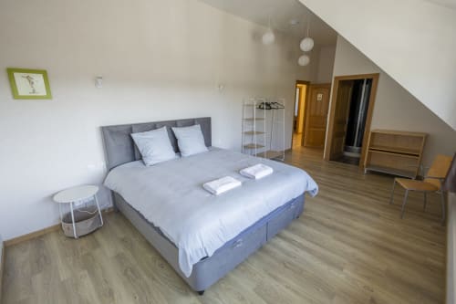 Chambre mansardée moderne à la Villa Chateaudine avec lit gris, draps blancs, parquet et vue sur le jardin à Châteaudun