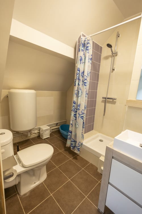 Salle de bains moderne à la Villa Chateaudine de l'hôtel Accolade à Châteaudun, avec douche, toilettes, lavabo et rideau à motifs bleus