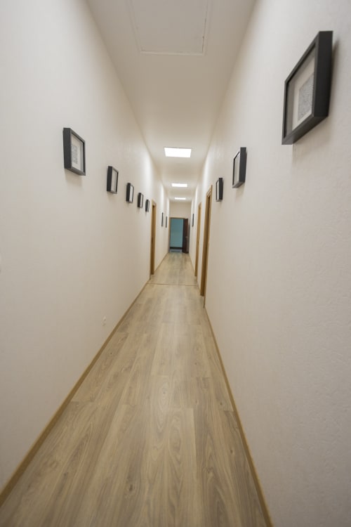 Couloir moderne de la villa Accolade à Châteaudun avec parquet, murs blancs, tableaux encadrés et éclairage contemporain