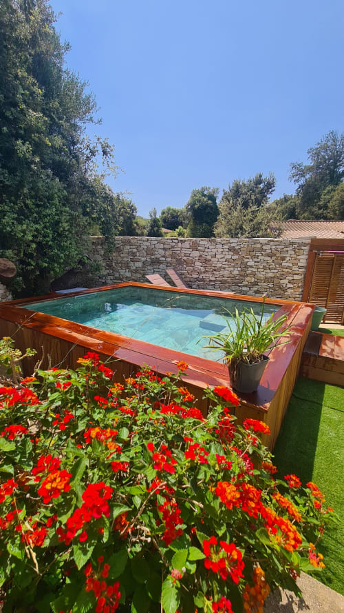 Piscine privée avec terrasse en bois et fleurs rouges dans le jardin de l'hôtel Perla Di Macchia, Bonifacio