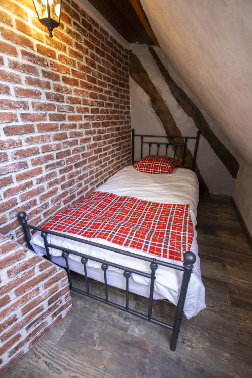 Chambre cosy sous les toits à l'hôtel Accolade à Châteaudun avec literie à carreaux rouges sur lit en métal noir contre mur de briques apparentes