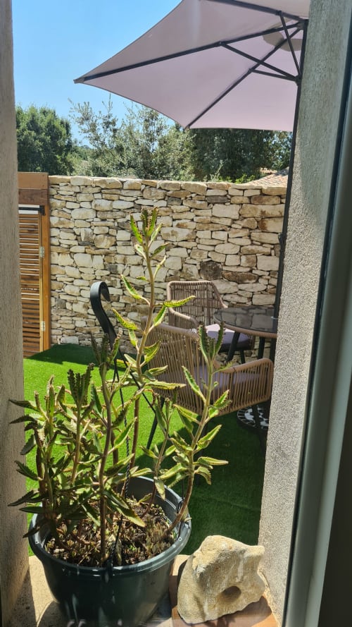 Terrasse de la suite Perla Di Macchia à Bonifacio avec plante en pot, mur en pierre, parasol violet et mobilier en rotin