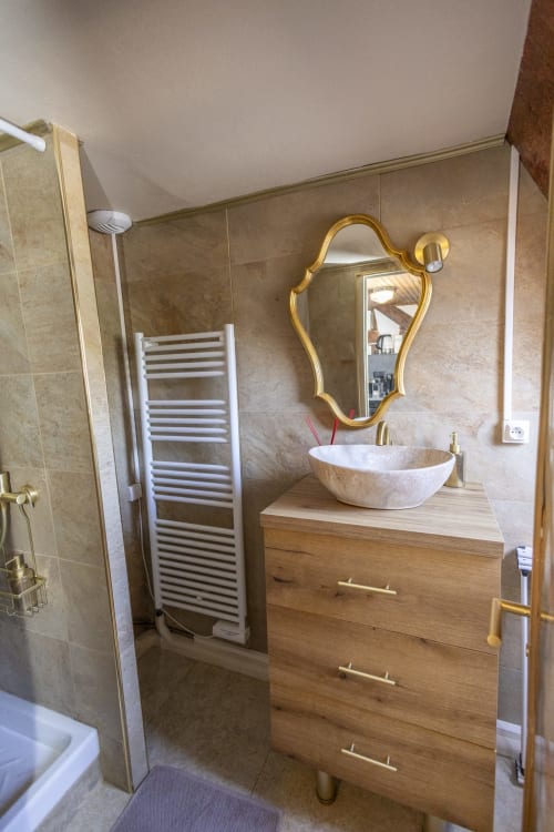 Salle de bain moderne avec vanité en bois, vasque en marbre blanc, miroir doré et murs carrelés à l'hôtel Accolade à Châteaudun.