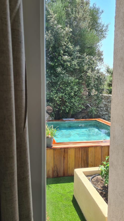 Piscine turquoise privée avec terrasse en bois à la suite de l'hôtel Perla Di Macchia à Bonifacio, entourée de verdure luxuriante
