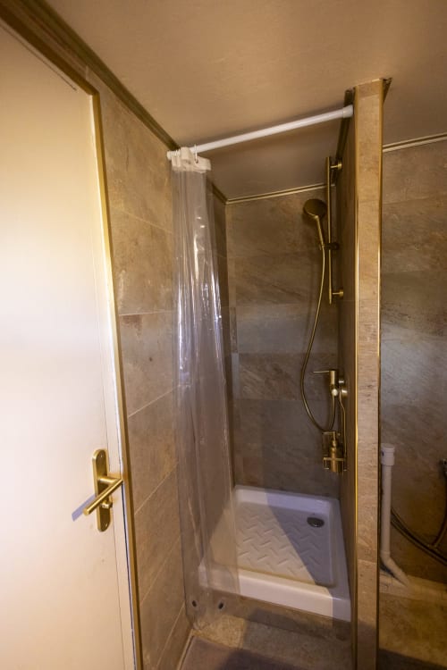 Douche moderne avec porte vitrée et robinetterie dorée dans la salle de bains de l'hôtel Accolade, Châteaudun