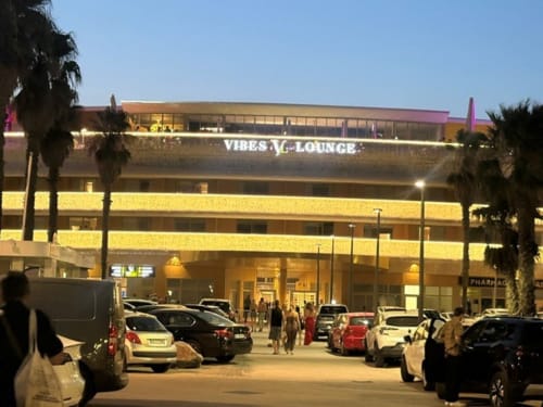 Vibes Lounge à Agde Luxury Loc à Cap d'Agde, vue extérieure en soirée avec palmiers et voitures garées