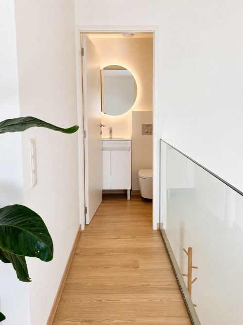 Corredor moderno de casa de banho na Terra Clara Studios, Esposende, com piso em madeira, paredes brancas, espelho redondo iluminado e