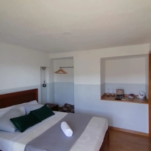 Quarto moderno em Tomás Barqueiro com cama de madeira, paredes brancas, detalhes azuis, casa de banho privativa e vista para o jardim do Douro.