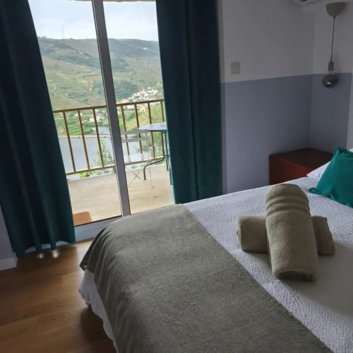 Quarto luminoso com assoalho de madeira, toalhas enroladas na cama, portas de terraço com vista para as montanhas do vale do Douro em Tomás