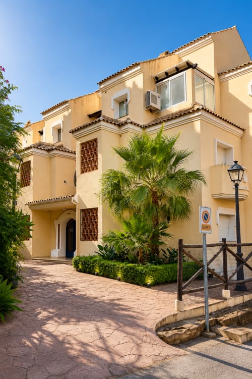 Fachada del hotel BH Marbella con exterior en color crema, tejado de barro, palmera y entrada pavimentada bajo cielo azul