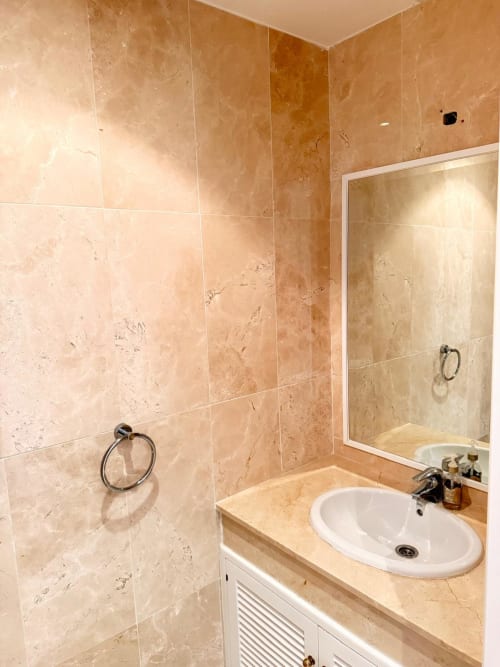 Baño moderno en BH Marbella con revestimiento de travertino, lavabo redondo blanco y cabina de ducha de cristal
