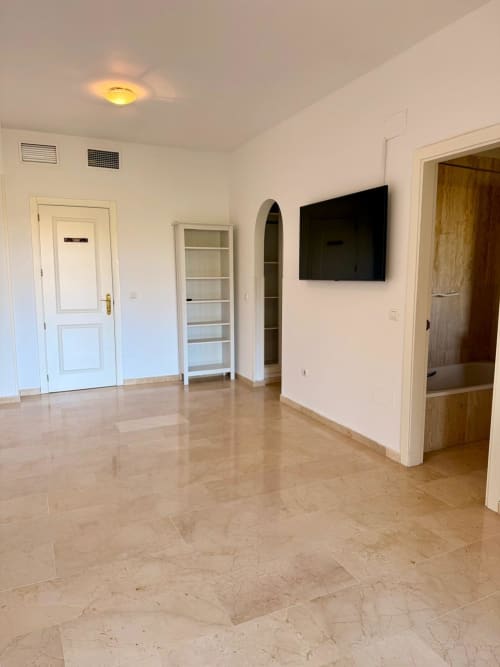 Amplio salón vacío en suite del hotel BH Marbella con suelos de mármol, TV, estanterías y múltiples accesos