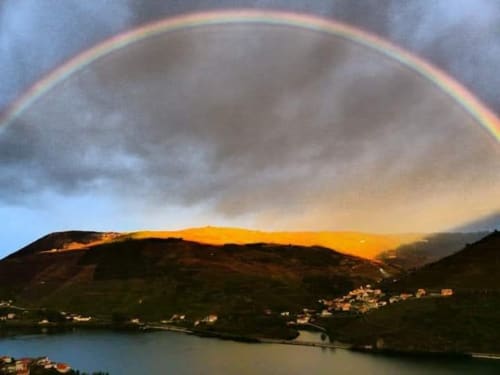 Arco-íris arqueando a paisagem do Vale do Douro com rio, montanhas e aldeia aninhada abaixo em Tomás Barqueiro
