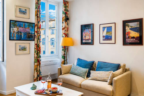 Elegant Nice apartment living room with vintage travel posters, blue accents, and Parisian-style windows overlooking the city