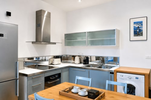 Modern kitchen in Enjoy Nice apartment with blue cabinetry, stainless steel appliances, and wooden dining table in Nice,