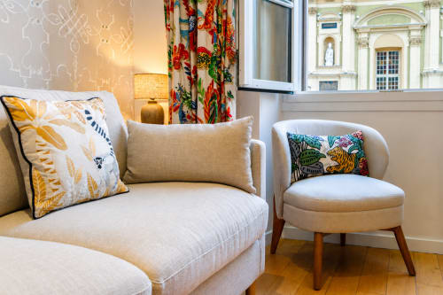 Elegant apartment seating area at Enjoy Nice with beige sofa, patterned pillows, round chair, and landmark view through