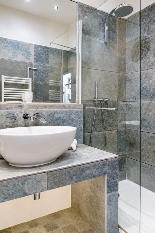 Modern bathroom in Enjoy Nice Rossetti apartment with grey marble tiles, round white soaking tub, walk-in shower, and chrome