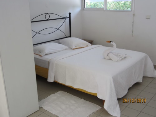 Chambre lumineuse du gîte Balaga Vacances à Sainte-Anne, avec literie blanche, tête de lit en métal et vue sur le jardin