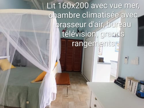 Chambre avec vue sur mer aux Colibris Amoureux : lit à baldaquin, climatisation, TV, bureau et rangements à Grand Bourg